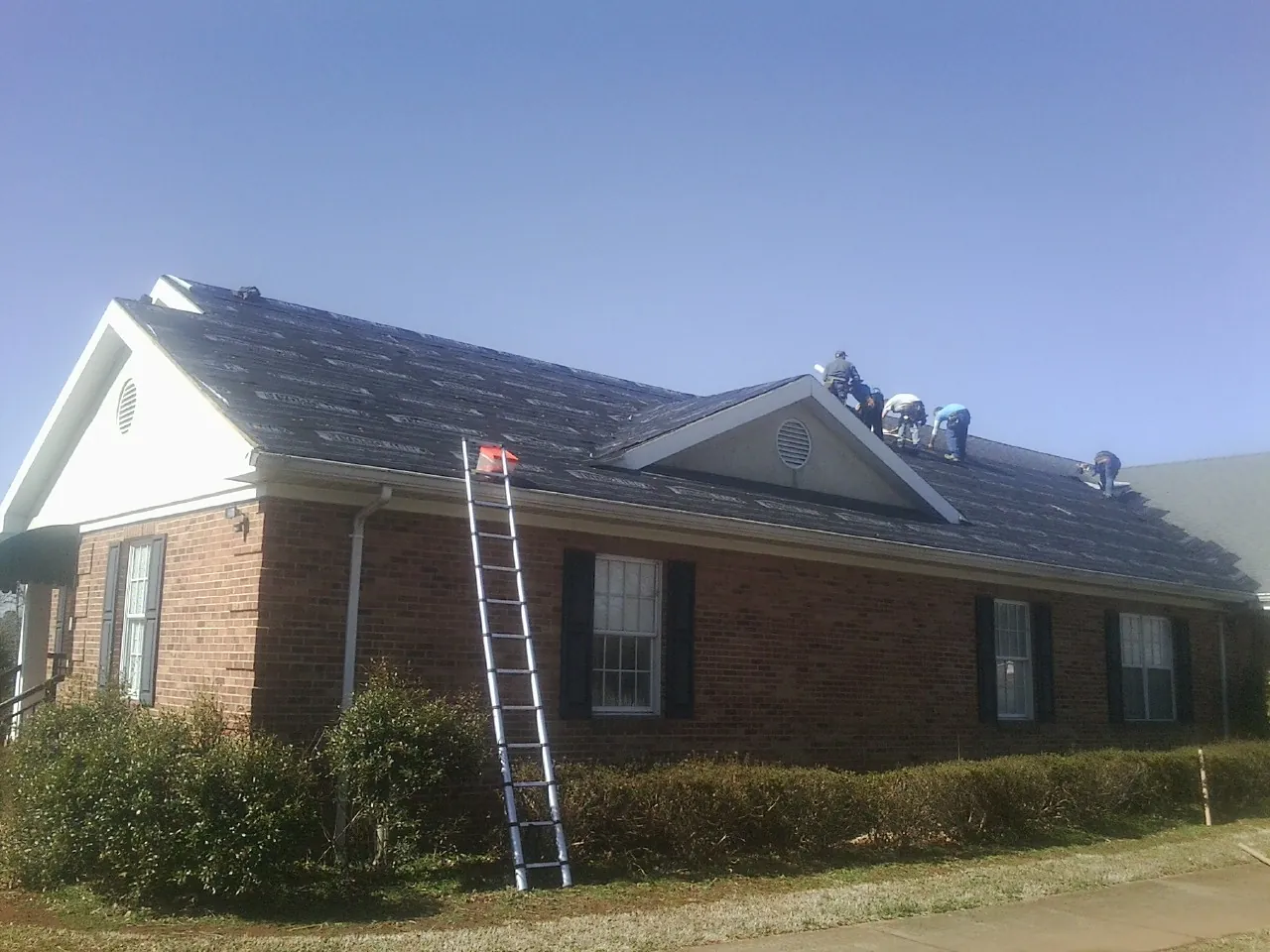 Crew tearing shingles off a brick ranch roof with a ladder set — Emergency Roof Repair work by our crew in Stowell
