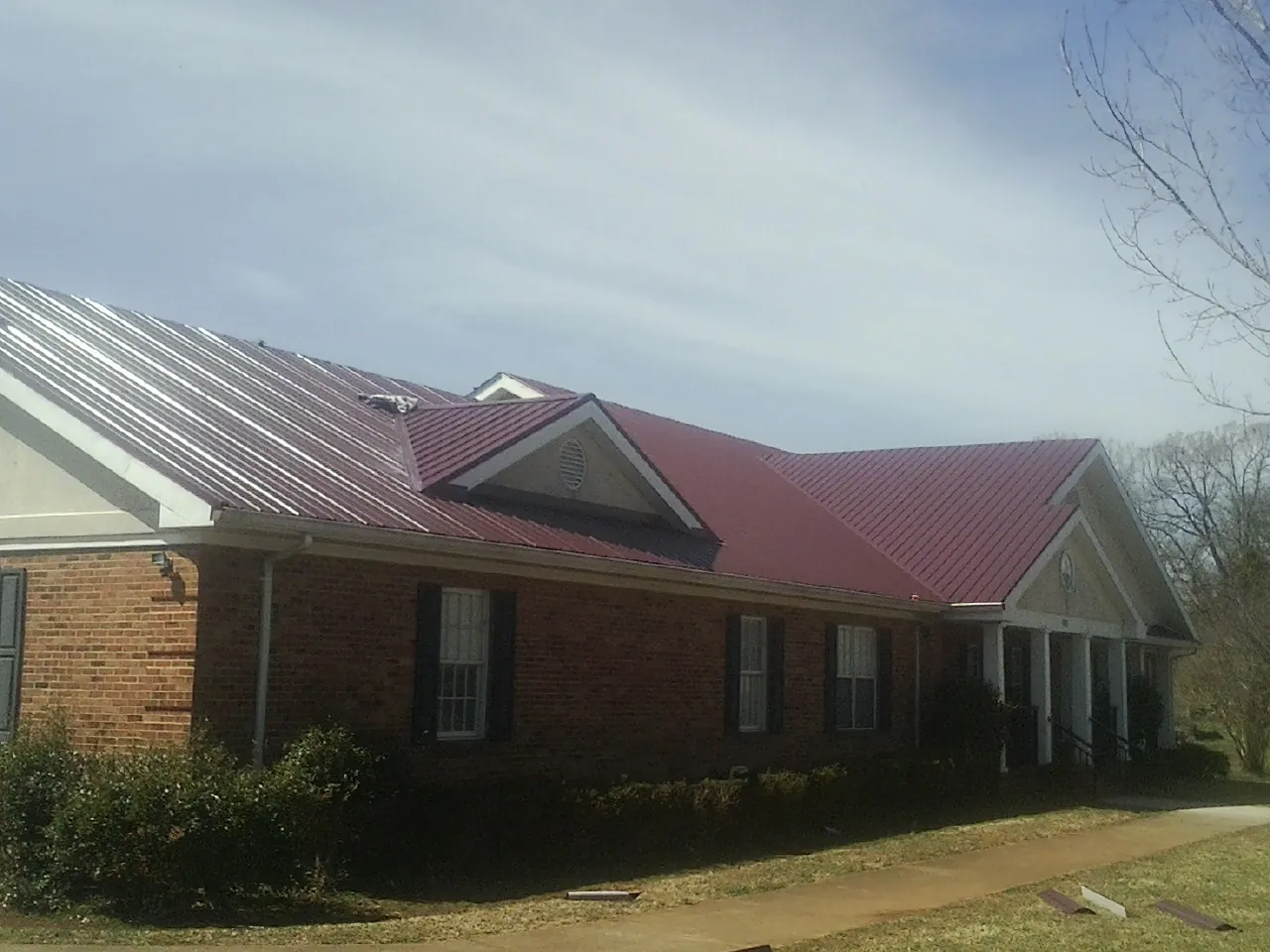 Red metal roof with gabled entries on a long brick building, from a Hail Damage Roof Repair job in Stowell