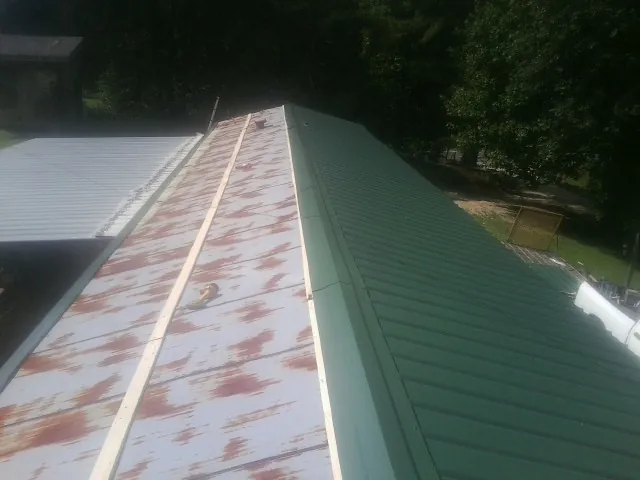 Old rusted panels beside newly installed green metal roofing — Wind Damage Roof Repair by Roofing Brothers in Stowell