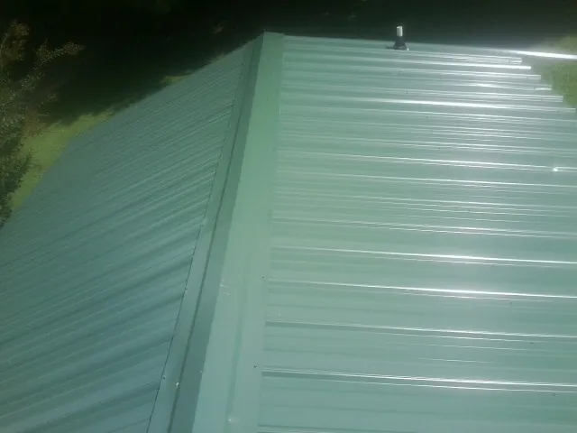 New green metal panels meeting at the ridge of a roof — Flat Roof Repair work by our crew in Stowell