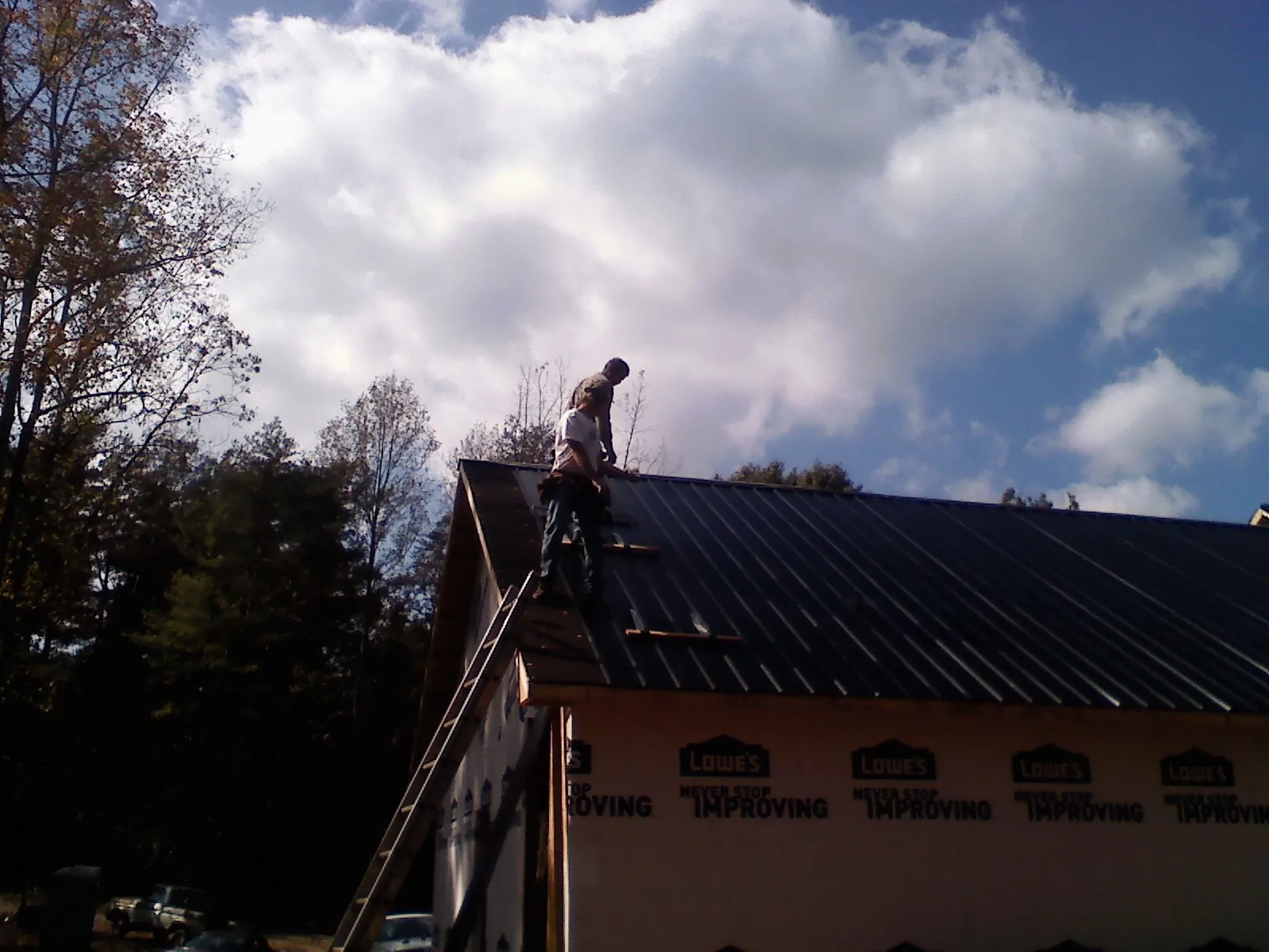 Roofer fastening dark metal panels high against a cloudy sky, from a Roof Inspection job in Stowell