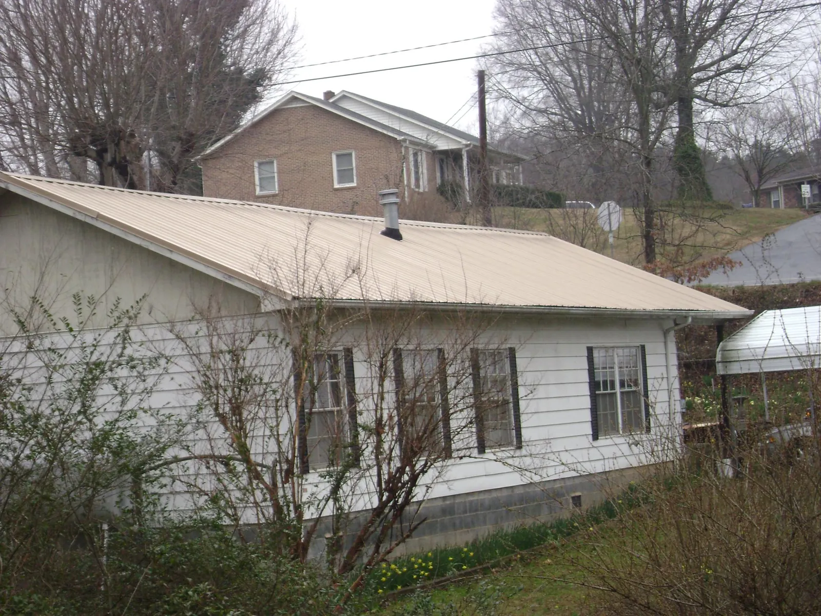 Tan metal roof on a white sided house set into a hillside — Commercial Roofing by Roofing Brothers in Stowell