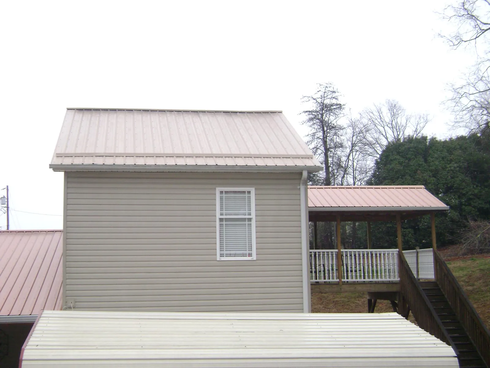 Tan metal roofs on a two story addition and attached porch, from a Roof Replacement job in Stowell